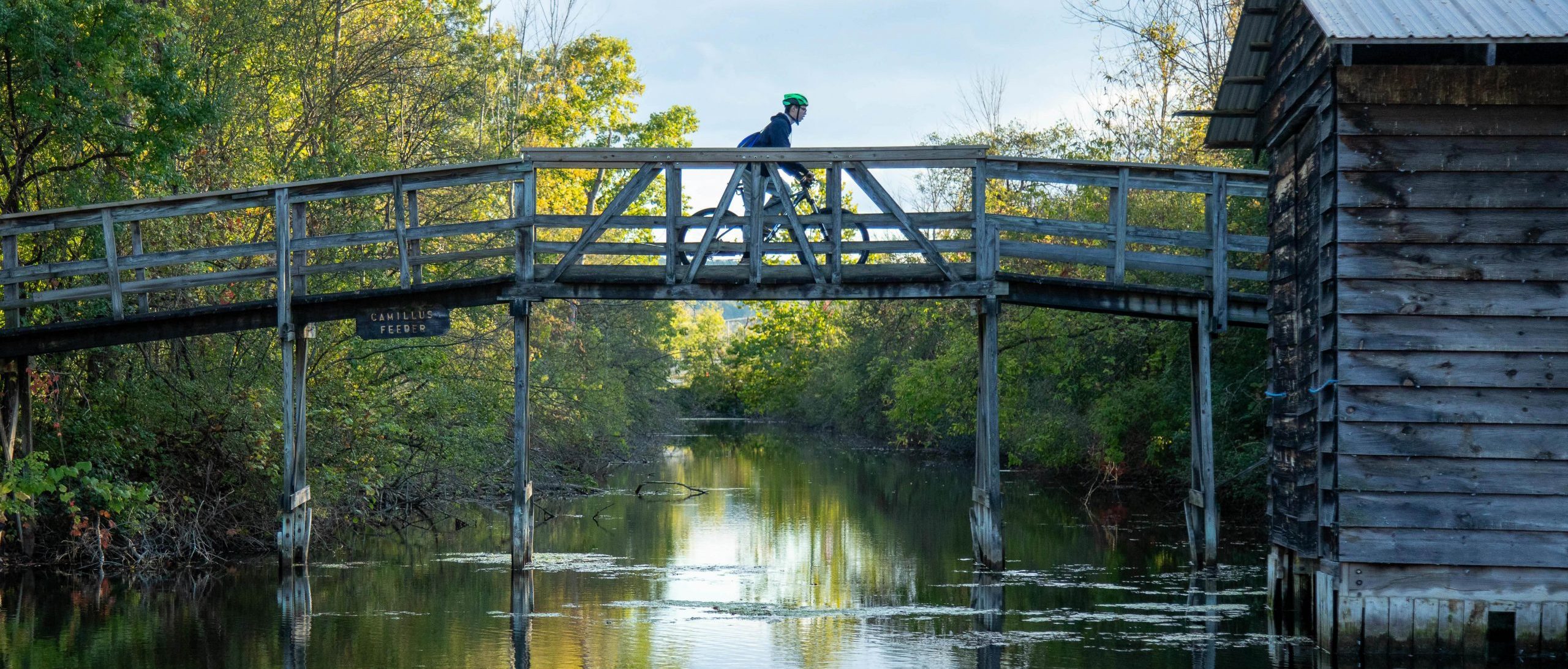 A cyclist crosses a woden bridge in the Camillus Erie Canal Park on October 10, 2024 near Camillus, New York. The bridge connects the Camillus feeder creek with the current canal expansion.