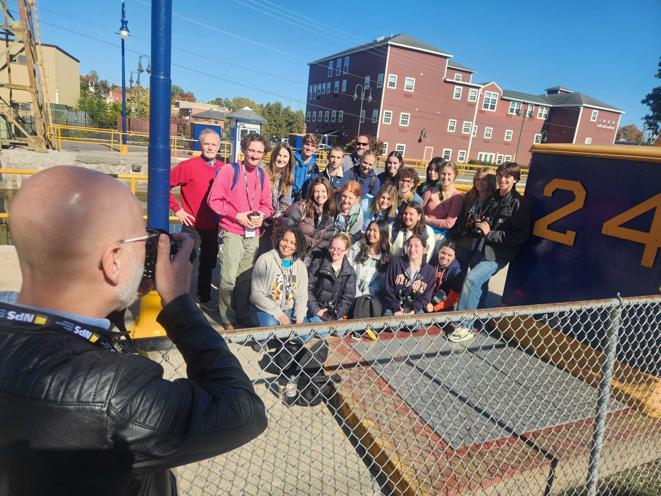 Newhouse Prof. Bruce Strong snaps a photo of the 2024 Alexia Fall Workshop Emerging Photographer Team members at Lock 24 in Baldwinsville, New York.